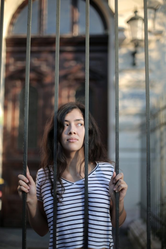 Photo by Andrea Piacquadio: https://www.pexels.com/photo/curious-isolated-young-woman-looking-away-through-metal-bars-of-fence-with-hope-at-entrance-of-modern-building-3808801/